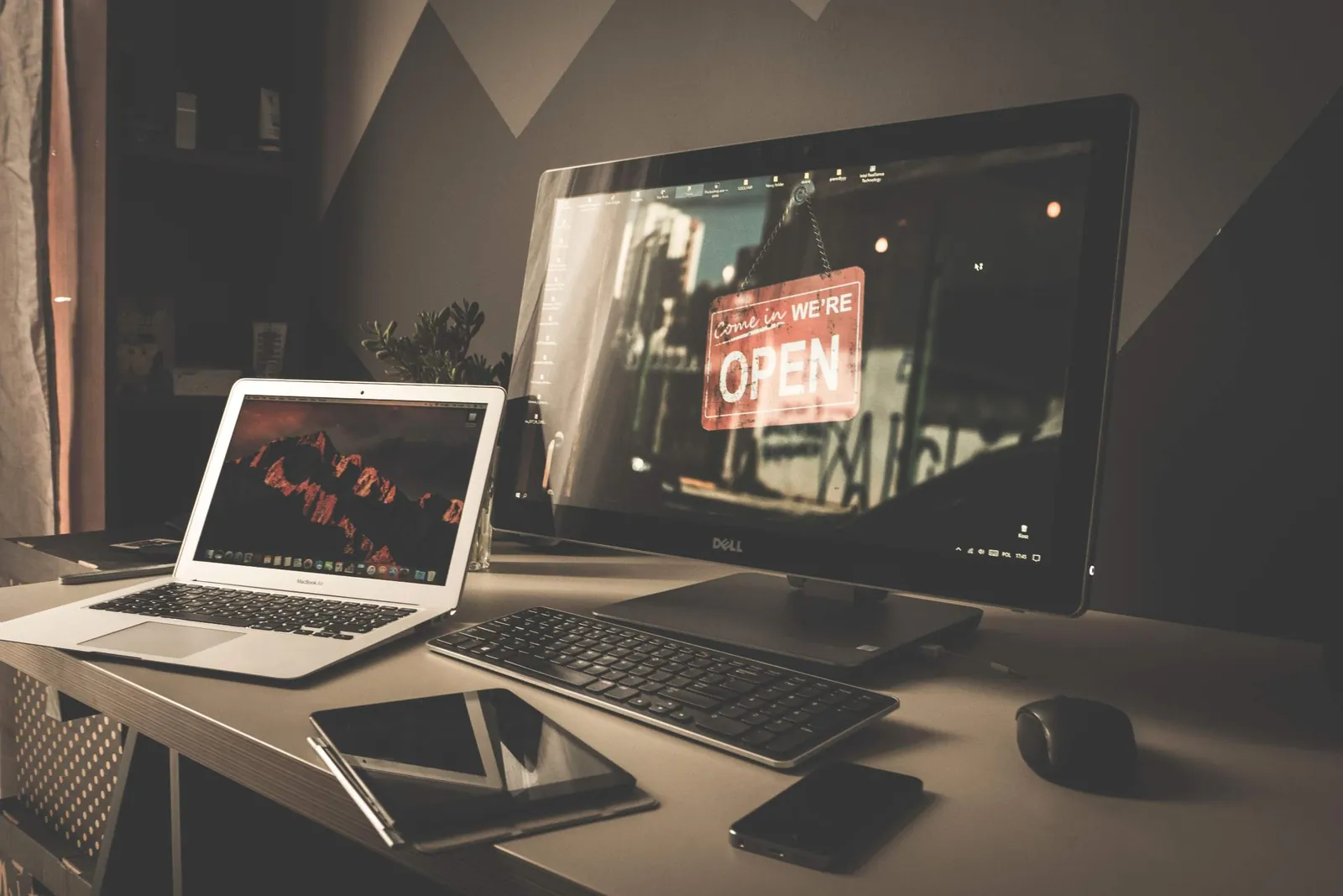 Meja kerja dengan monitor yang menampilkan papan "We're open" sebuah toko, di samping laptop, keyboard, tablet, dan ponsel: perangkat yang dipakai pelanggan untuk membuka sebuah situs web.